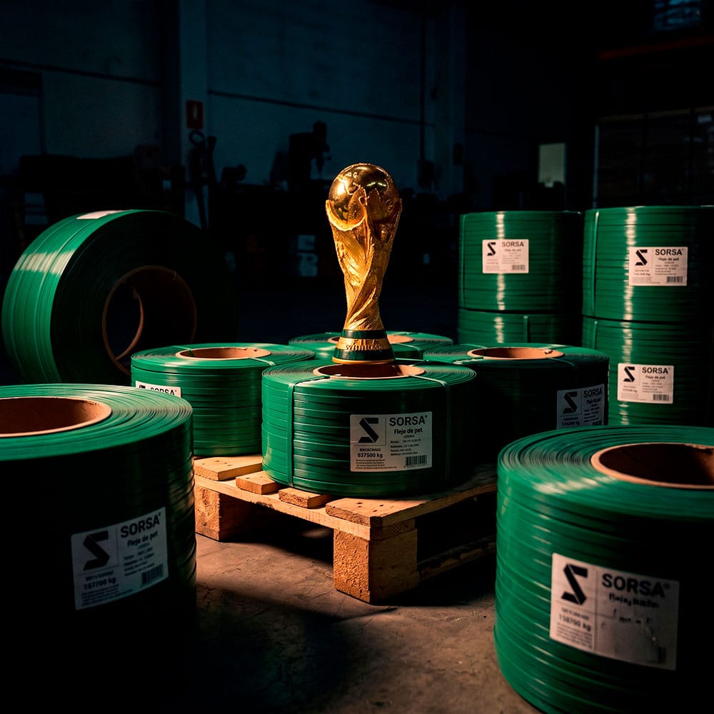 Copa del Mundo de fútbol colocada sobre un palet de rollos de fleje PET verde de la marca Sorsa en una fábrica de embalaje en España.